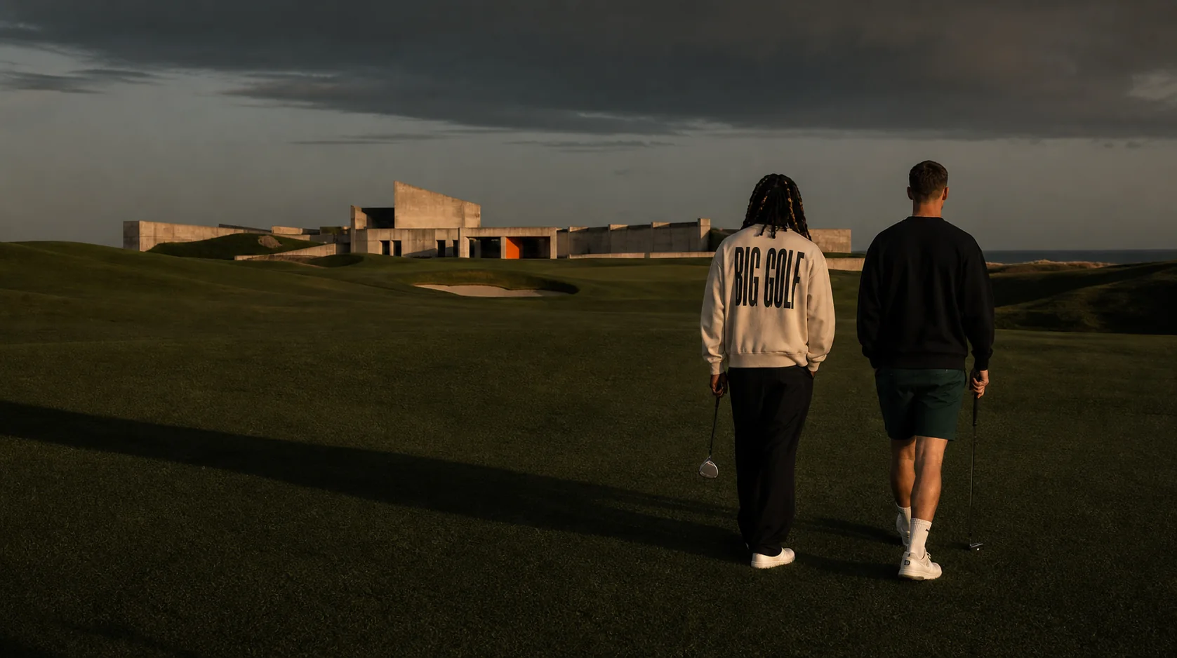 Two golfers crossing a vast fairway toward a modern clubhouse